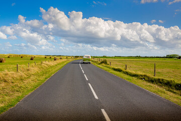 Fototapeta na wymiar Road in the middle of natural landscape with a van car on the road with blue cloudy sky background