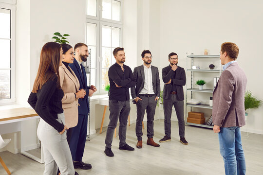 Group of business people listening to their colleague or their leadership at the working place. Company employees talking in a meeting standing in office. Cowokers greeting new employee.