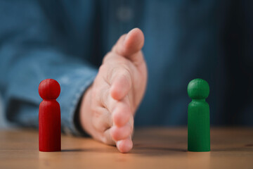 Palm hand blocking and divide between red and green wooden figure for resolving conflict and mediate management concept.