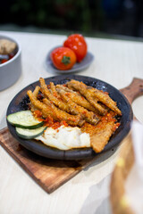 Close up sambal gami ceker or fried chicken feet with sambal cooked in earthenware plate against wooden background. Served on wooden table with chili, spoon and fork as decoration