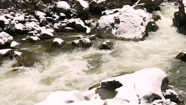 Stunning winter landscape of a mountain river flowing through rocky terrain, perfect for nature scenes.