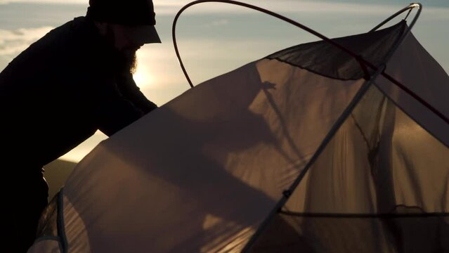 A man struggling to erect a tent in strong windy and bright sunshine
