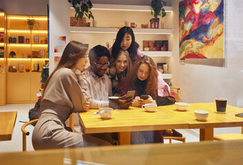 Multiracial happy young people, black and white cheerful comrades laughing, enjoying food, having fun sitting together at a table in a restaurant, different friends sharing lunch at a meeting