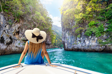 A blonde tourist woman with hat sits on a boat and enjoys the scenery of the beautiful Phi Phi islands in Krabi, Thailand
