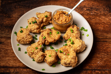 Cauliflower wings food. Pieces of cauliflower cooked in batter on a plate on a wooden background. Sprinkled with green onions.