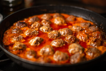 Cooking homemade meatballs in a frying pan in a sauce of tomatoes and sour cream.