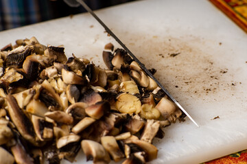 Sliced champignon mushrooms on a cutting board. Women's hands cut mushrooms with a knife.