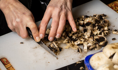 Sliced champignon mushrooms on a cutting board. Women's hands cut mushrooms with a knife.
