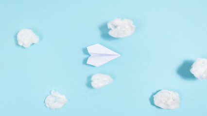 White paper airplane flies through white clouds on a blue background.