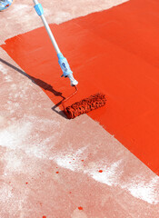 Worker waterproofing the terrace of the building with red rubber waterproofing paint spread with a roller