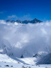Fototapeta na wymiar snow covered mountains in winter with stormy clouds touching it. Vibrant blue sky and mountains 