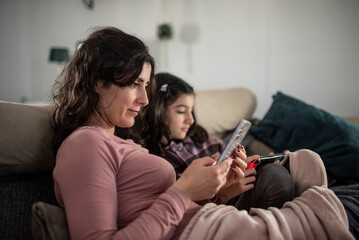 Mother and daughter looking phone at home sofa covered with blankets