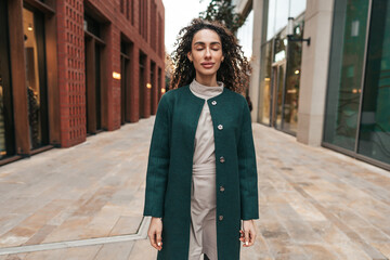 Portrait of young woman in green coat with curly hair in the city
