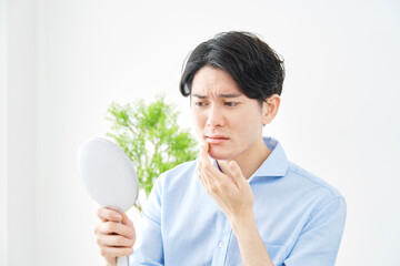 鏡を見て肌荒れに悩む男性