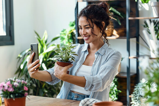 Shot of beautiful smiling woman taking photos with smartphone to plants and flowers in a greenhouse