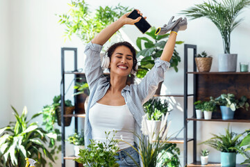 Beautiful smiling woman arranging plants and flowers while dancing in a greenhouse