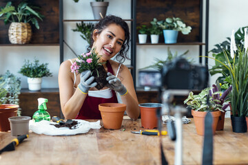 Influencer woman arranging plants and flowers while recording a tutorial video with smartphone in a greenhouse