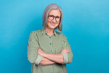 Photo of confident pretty senior lady assistant dressed striped shirt eyewear arms crossed isolated blue color background