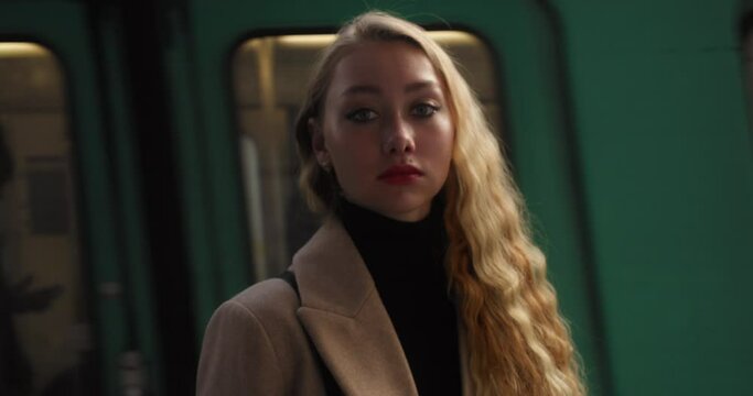 Glamorous Fierce Woman With Blonde Wavy Hair Turns Around And Looks At Camera With Moving Train In Background. medium shot