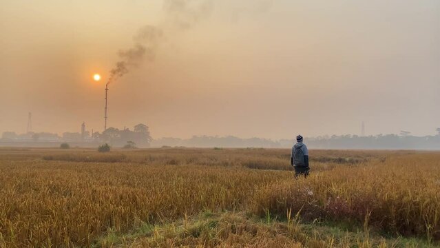 Photographer walking on dry field by polluting gas plant, holding DSLR camera