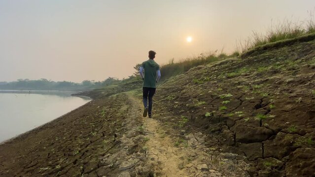 Man jogging by river bed in Sylhet, Bangladesh, rear wide view, sunset