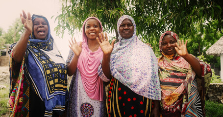 A Group of Authentic African Women in Traditional Clothes Waving and Smiling at the Camera. Friendly Female Rural Villagers Welcoming People in their Village with Big Smiles and Open Hearts - obrazy, fototapety, plakaty
