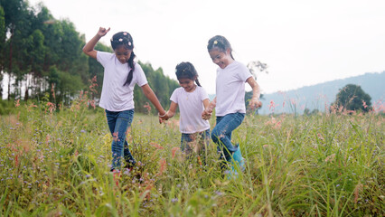 Three active sister cute child girls hold hands move way forward go walk in rural green grass...