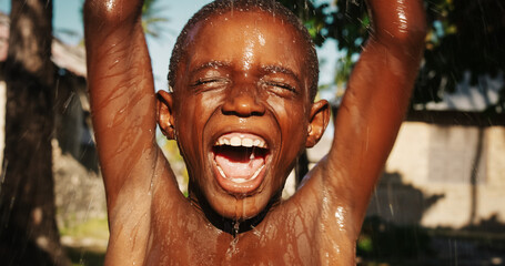 Portrait of an African Little Boy Jumping and Dancing Under Pouring Water. Happy and Innocent Black...