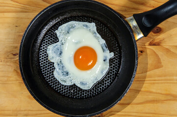 Cooking roasted eggs for breakfast, another egg is driven into pan for fried eggs.