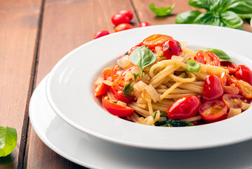 Piatto di deliziosi spaghetti conditi con olio di oliva, pomodori datterini e basilico fresco,...