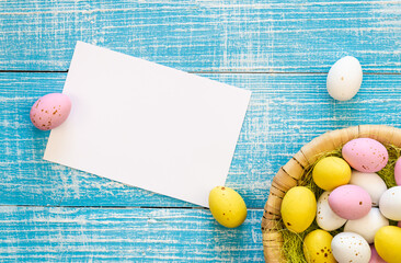 Easter background with colorful chocolate eggs and a blank piece of paper, on a blue wooden background, flat lay, Easter holiday concept, copy space.