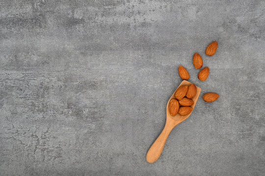 Almond in spoon and group of almond nuts on stone texture background. Top view.