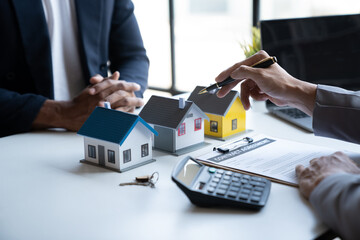 Two young Asian businessmen or architects are describing architectural house model in their office together for the construction of  housing estate project in  prime location the location is perfect