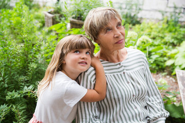 Naklejka premium grandmother and little granddaughte hag and having fun together in the garden. Happy family enjoying summer outdoors.