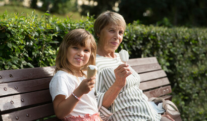 grandmother and child granddaughter eat ice cream in the park on a summer day. happy family has fun...