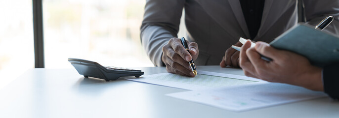 Fototapeta premium Two young Asian businessmen analyzing Calculate and discuss and brainstorm data, charts, graphs Taking notes on financial reports in notebooks at office financial advisors and accounting concepts.