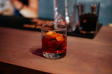 Glass of negroni alcohol cocktail stands on a bar table with a piece of orange peel