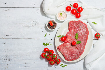 Raw veal steak with spices, cherry tomatoes. Trendy hard light, dark shadow, white wooden background