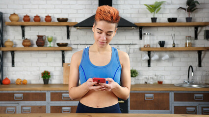 Lady with haircut surfs internet with phone in kitchen