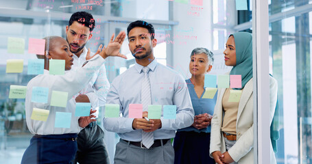 Meeting, collaboration and sticky notes with a business man training a team while planning strategy on glass in an office. Teamwork, diversity and workshop with a man and woman employee group at work