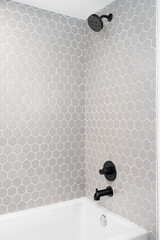 A shower detail with brown textured hexagon tiles, white bathtub, and black showerhead and faucet.