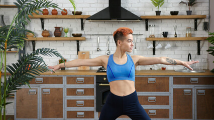 Woman blogger with haircut does yoga exercises in kitchen