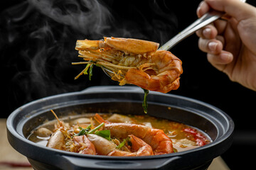 Tom Yam Kung or Tom Yum soup is Thai hot spicy soup shrimp or prawn with lemon grass, lemon, galangal, mushrooms, coconut milk and chili in bowl on wooden table top view, famous Thai food cuisine.