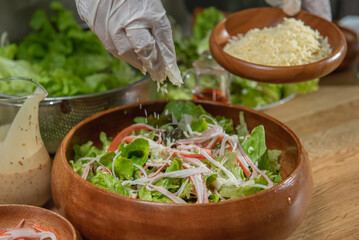Hand chef sprinkle parmesan cheese shredded on caesar salad in wood blow. Caesar salad or green salad in wood blow must sprinkle by parmesan cheese shredded. parmesan cheese shredded is mix  © BESTIMAGE