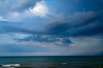 Naklejka na ściany i meble The sea is in front of a thunderstorm. Rain strip over the sea. Clouds in the blue sky