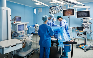 Group of concentrated surgeons while surgical operation in operating theater with nurses and...