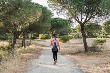 Fototapeta premium Back view of woman with pink shirt and backpack walking on a path in a forest