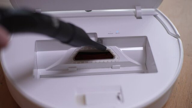 Close-up cropped shot of unrecognizable man hoovering with regular wired vacuum cleaner the inside of robot vacuum cleaner, slow motion. Concept of maintenance modern home appliance.