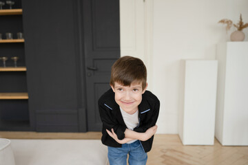 Portrait of a happy preschool boy in a black shirt in the interior of an apartment near a white sofa.