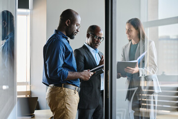 Young businessman preparing report while standing by his boss and female colleague showing document to director of company